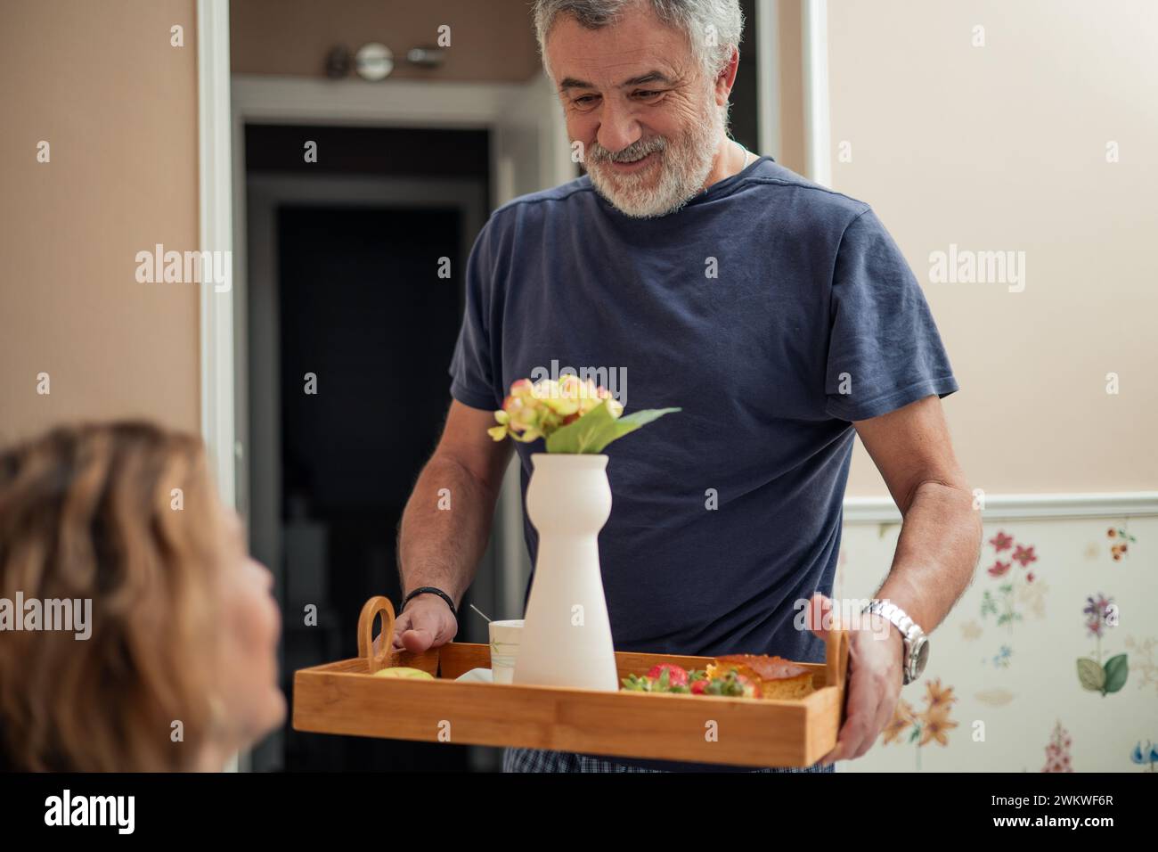 In questo primo piano, assistiamo ad un momento di trepidazione tra una coppia in pensione. Il marito sta accanto al letto, tenendo tenero un vassoio carico Foto Stock