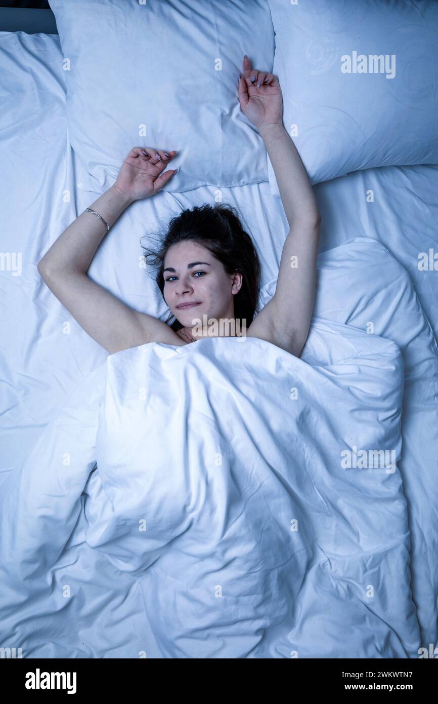 Una bella ragazza dorme in un letto con una lenzuola bianche Foto Stock