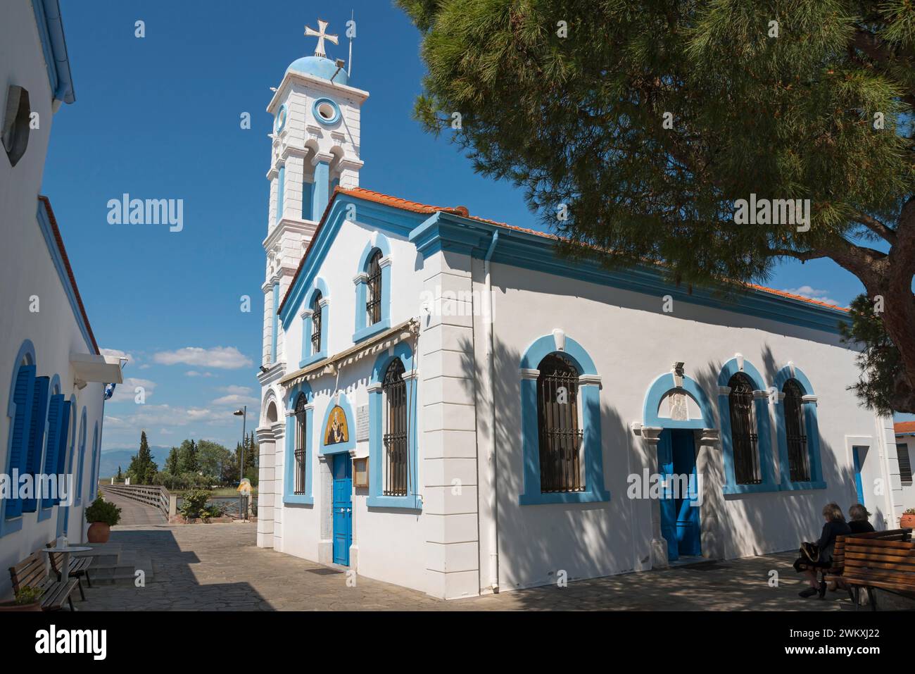 Chiesa in una giornata di sole, persone sedute sulle panchine del parco all'ombra, Monastero di San Nicola, Monastero di Agios Nikolaos, Agiou Nikolaou, Vistonidas Foto Stock