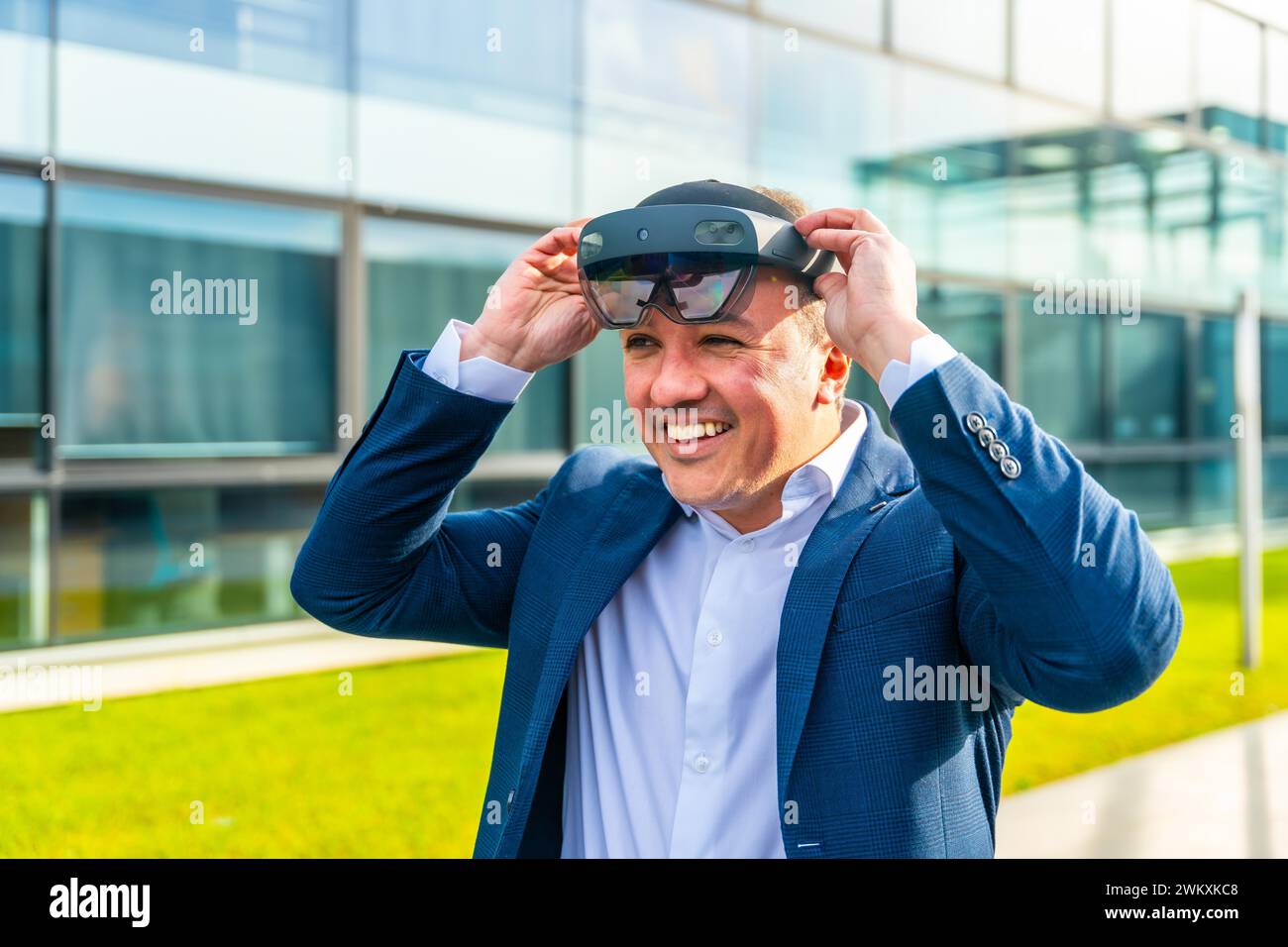 Uomo d'affari felice che indossa un visore per la realtà virtuale all'esterno di un edificio finanziario Foto Stock