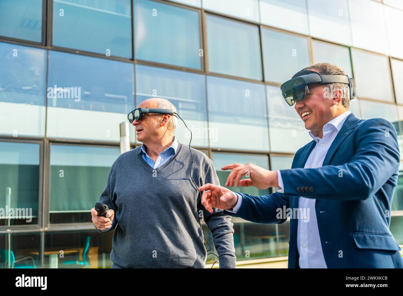 Uomini d'affari anziani e maturi che utilizzano il visore VR con azioni all'aperto accanto a un edificio finanziario Foto Stock