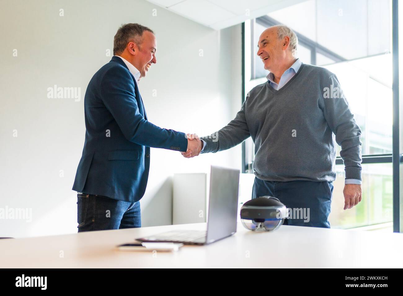 Gli uomini d'affari concludono un accordo su un innovativo occhiale di protezione per la realtà mista che stringe la mano in ufficio Foto Stock