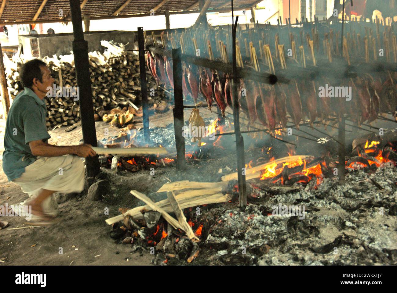Un lavoratore mantiene la distribuzione equa delle bucce di cocco utilizzate come combustibile per fumare le carni di tonno striato in un'industria domestica a Bitung, Sulawesi settentrionale, Indonesia. I contributi delle conoscenze indigene all'innovazione tecnologica offrono un'ampia gamma di opzioni per la gestione, tra l'altro, della sicurezza alimentare, secondo la relazione del 2023 del gruppo intergovernativo sui cambiamenti climatici (IPCC). Popolarmente noto come cakalang fufu, il tonno affumicato è considerato un alimento esotico indigeno e potrebbe diventare una soluzione alternativa per affrontare gli impatti del cambiamento climatico sull'oceano. Foto Stock