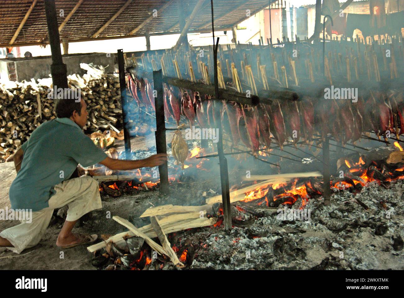 Un lavoratore mantiene la distribuzione equa delle bucce di cocco utilizzate come combustibile per fumare le carni di tonno striato in un'industria domestica a Bitung, Sulawesi settentrionale, Indonesia. I contributi delle conoscenze indigene all'innovazione tecnologica offrono un'ampia gamma di opzioni per la gestione, tra l'altro, della sicurezza alimentare, secondo la relazione del 2023 del gruppo intergovernativo sui cambiamenti climatici (IPCC). Popolarmente noto come cakalang fufu, il tonno affumicato è considerato un alimento esotico indigeno e potrebbe diventare una soluzione alternativa per affrontare gli impatti del cambiamento climatico sull'oceano. Foto Stock