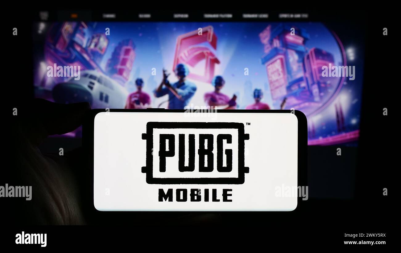 Persona che tiene un cellulare con il logo del videogioco Battle royale PUBG Mobile davanti alla pagina Web dell'azienda. Mettere a fuoco il display del telefono. Foto Stock