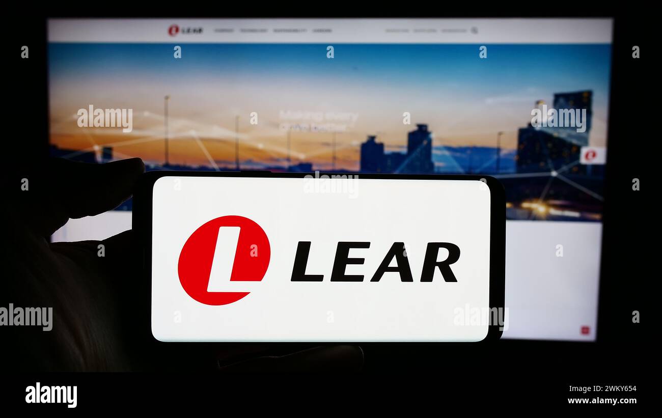 Persona che possiede uno smartphone con il logo della società di fornitura automobilistica statunitense Lear Corporation davanti al sito Web. Mettere a fuoco il display del telefono. Foto Stock