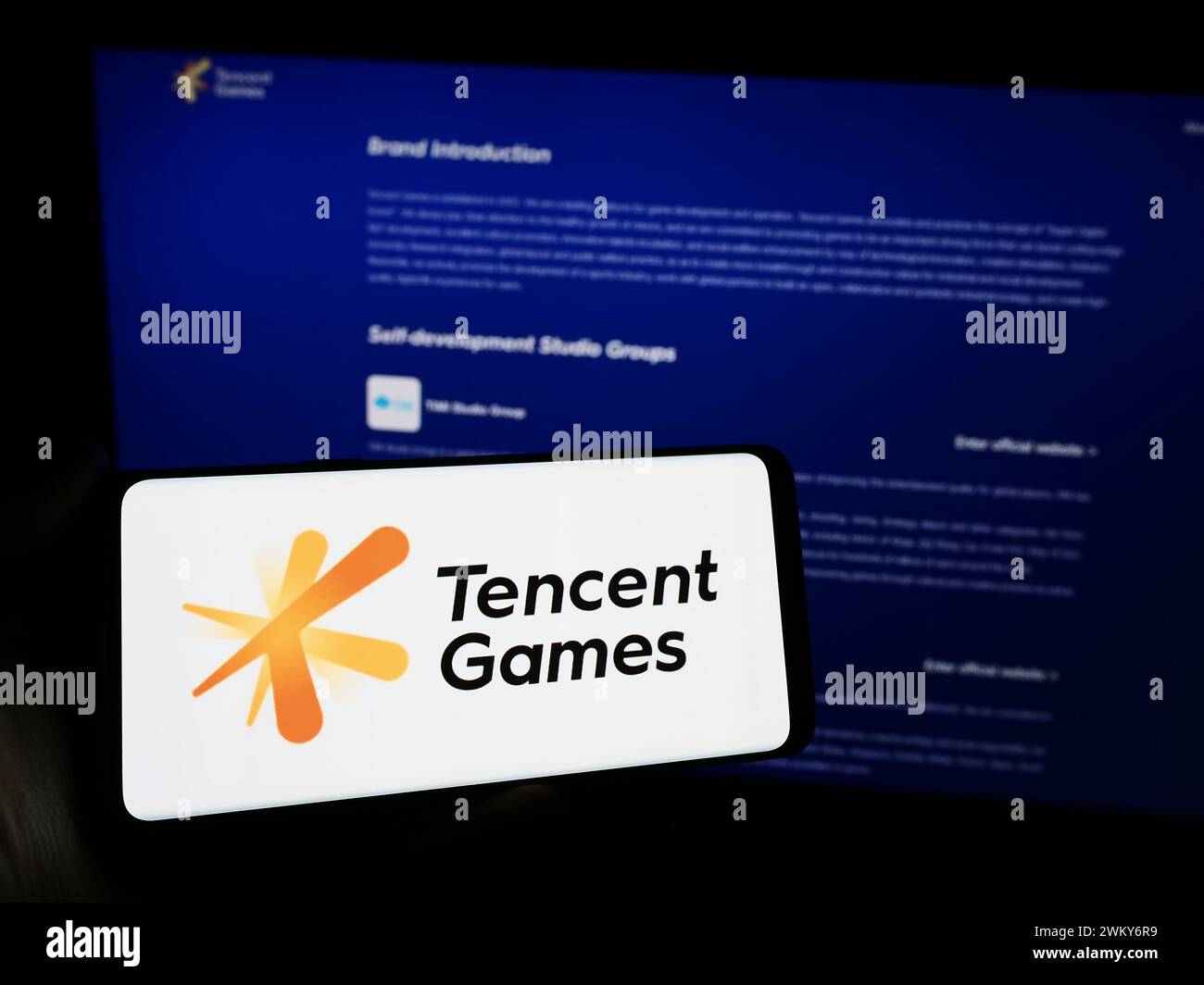 Persona che detiene un cellulare con il logo della società cinese di videogiochi Tencent Games davanti alla pagina web aziendale. Mettere a fuoco il display del telefono. Foto Stock