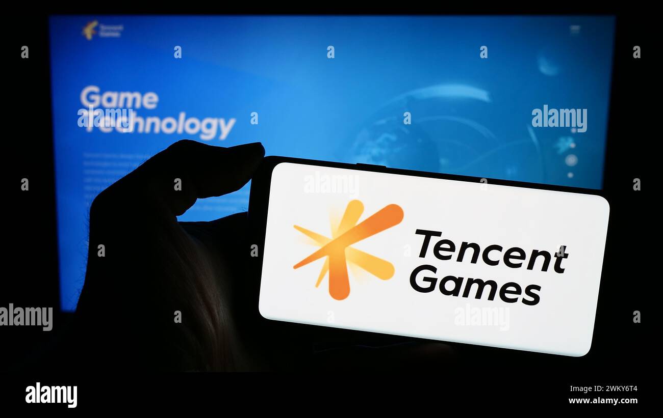 Persona che possiede un telefono cellulare con il logo della società cinese di videogiochi Tencent Games di fronte alla pagina Web aziendale. Mettere a fuoco il display del telefono. Foto Stock