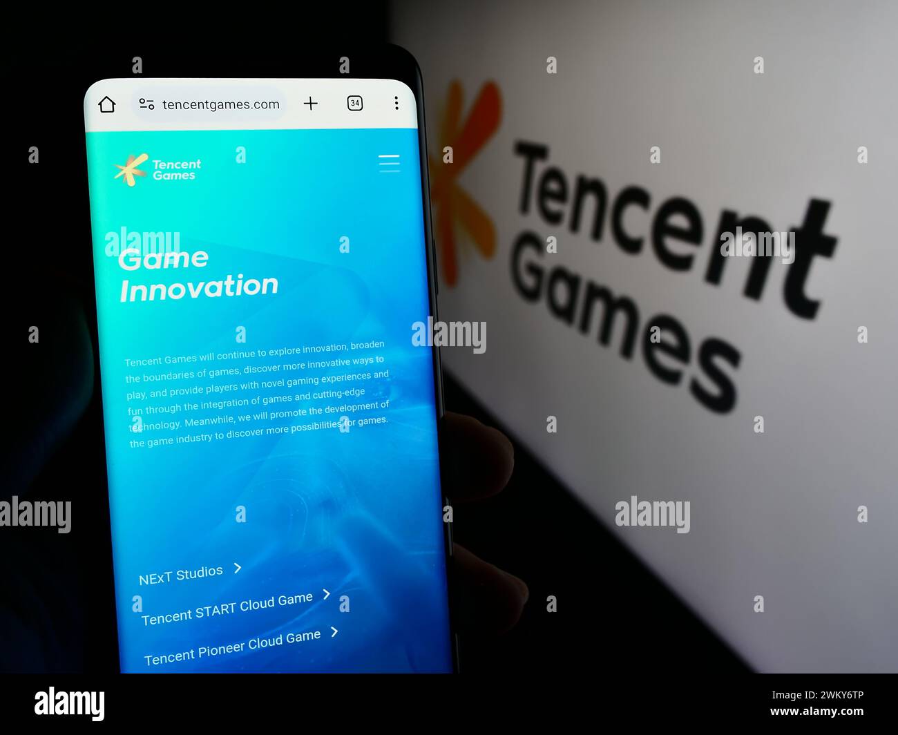 Persona che detiene un cellulare con pagina web della società cinese di videogiochi Tencent Games davanti al logo aziendale. Messa a fuoco al centro del display del telefono. Foto Stock