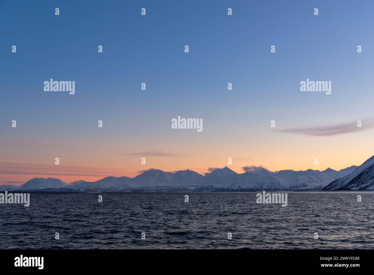 Europa, Norvegia, Tromso, Troms County, le Alpi Lyngen attraverso Ullsfjorden all'alba con una barca distante per l'avvistamento delle balene Foto Stock