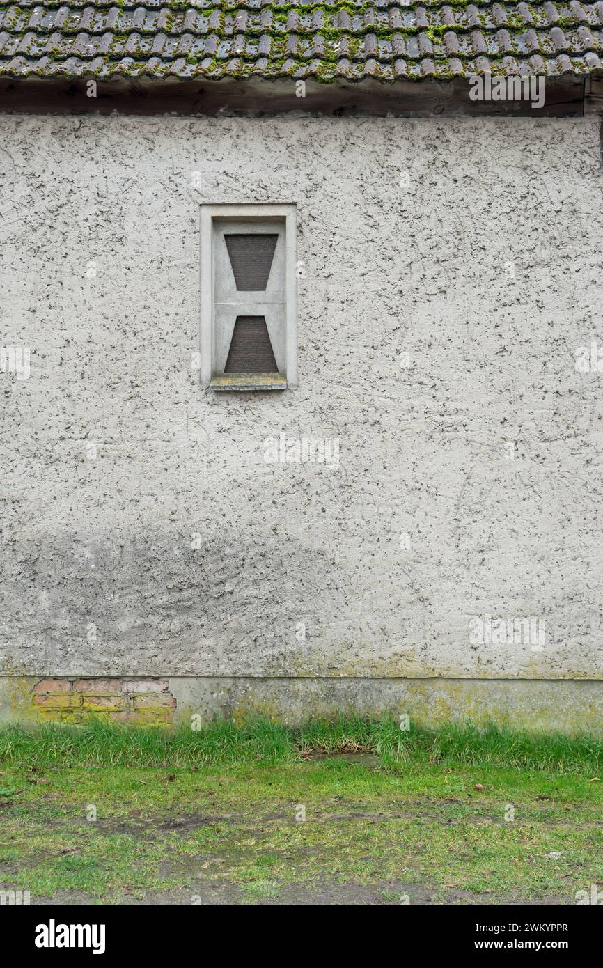 Parete esterna grigia con intonaco lavato e una piccola finestra in blocchi di vetro Foto Stock