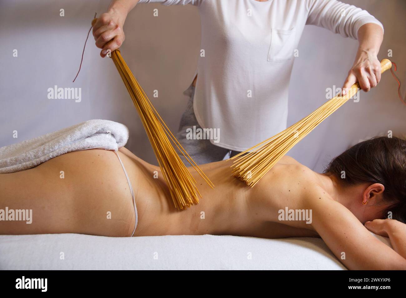 Massaggio schiena nella sala massaggi con scopa in bambù. Massaggiatore massaggiatore schiena donna con bambù. Vista laterale orizzontale, massaggio rilassante Foto Stock