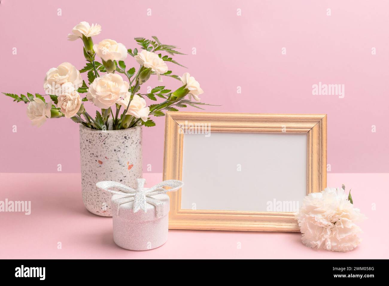 Bouquet di garofani gialli in un vaso, una confezione regalo e una cornice fotografica con spazio per le copie sullo sfondo rosa. Foto Stock