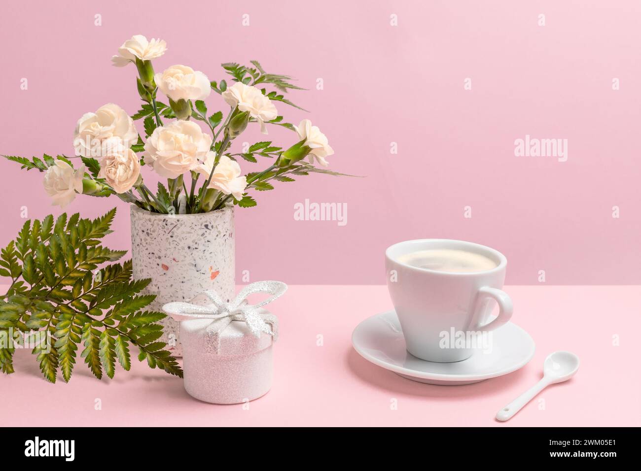 Bouquet di garofani gialli in un vaso, una confezione regalo e una tazza di caffè sullo sfondo rosa. Foto Stock