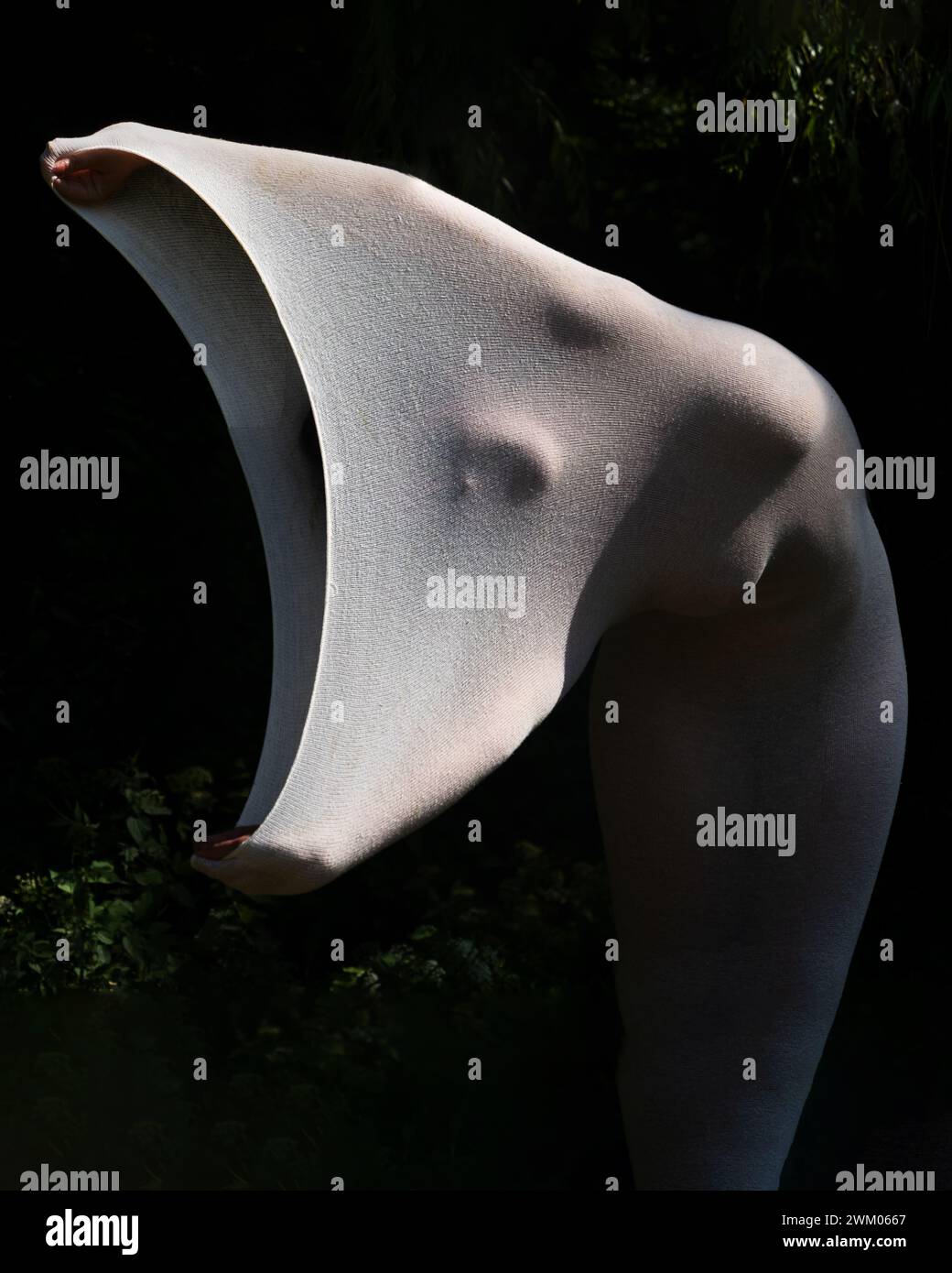 foto artistica di una giovane donna nuda, sexy ed elegante, il suo corpo avvolto in un abito bianco stretto a pelle lunga che mette in risalto le forme del corpo, come una statua vivente in natura Foto Stock