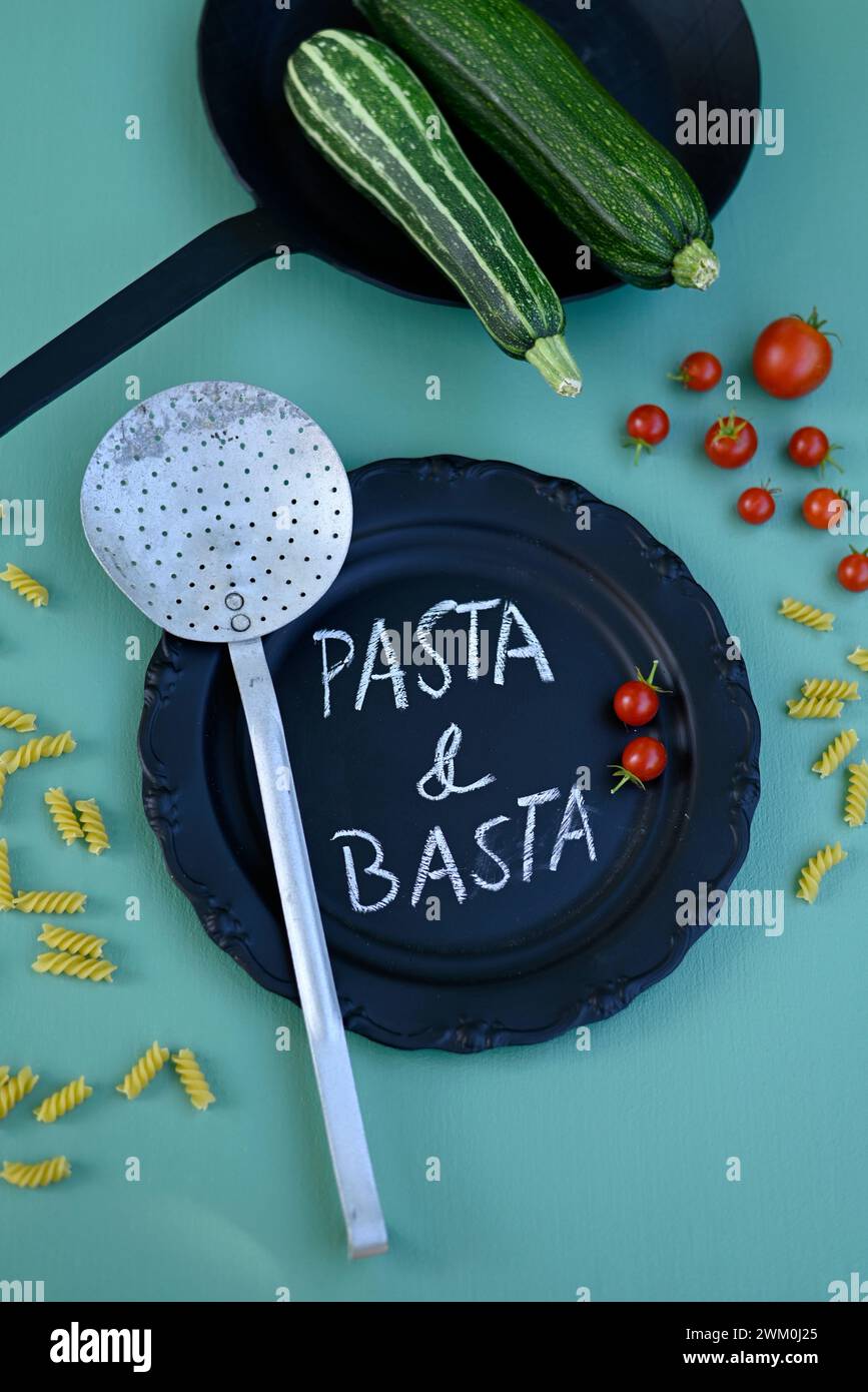 Bicchierino di verdure, pasta, setaccio, padella e piatto nero con frase breve scritta in gesso Foto Stock