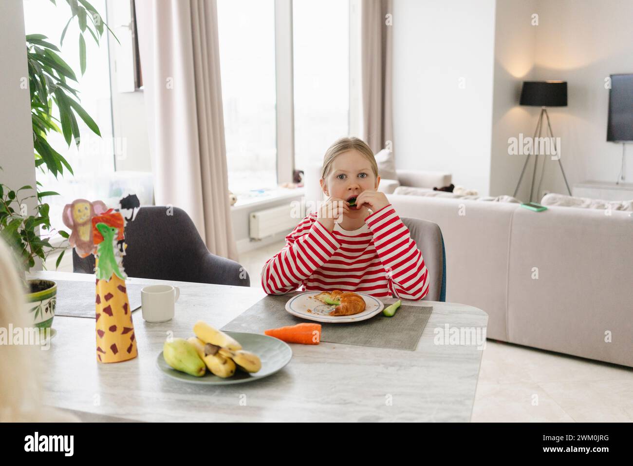 Ragazza che fa colazione al tavolo da pranzo nel soggiorno di casa Foto Stock