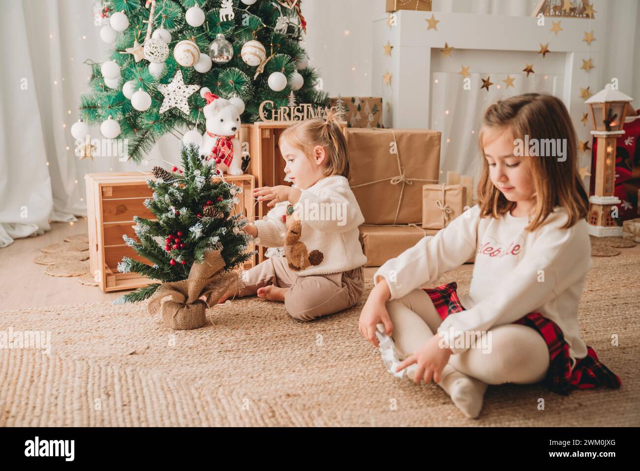 Ragazza con sorella che decora un piccolo albero di Natale a casa Foto Stock