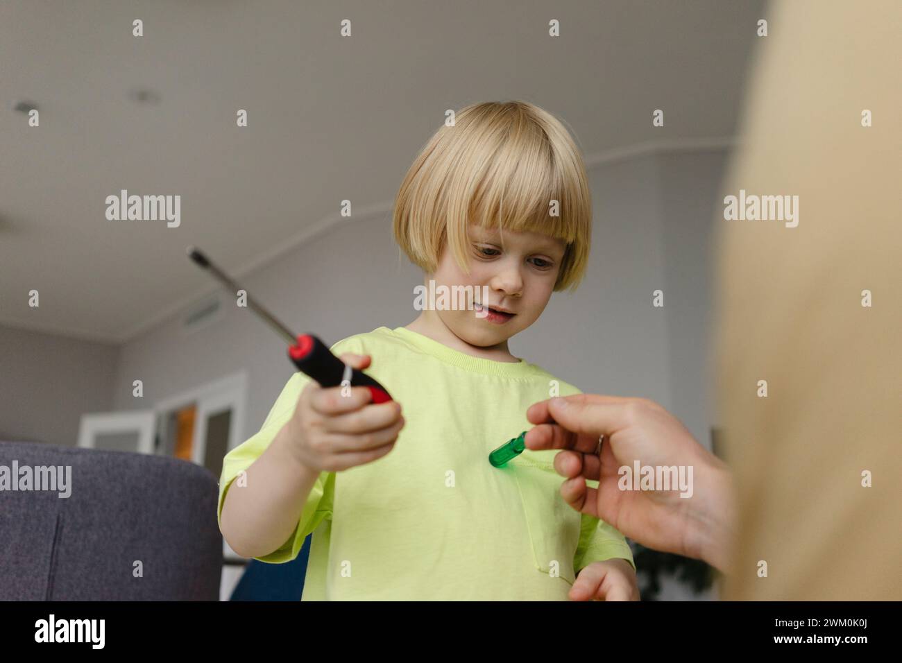 Bambino che tiene il cacciavite vicino al padre a casa Foto Stock