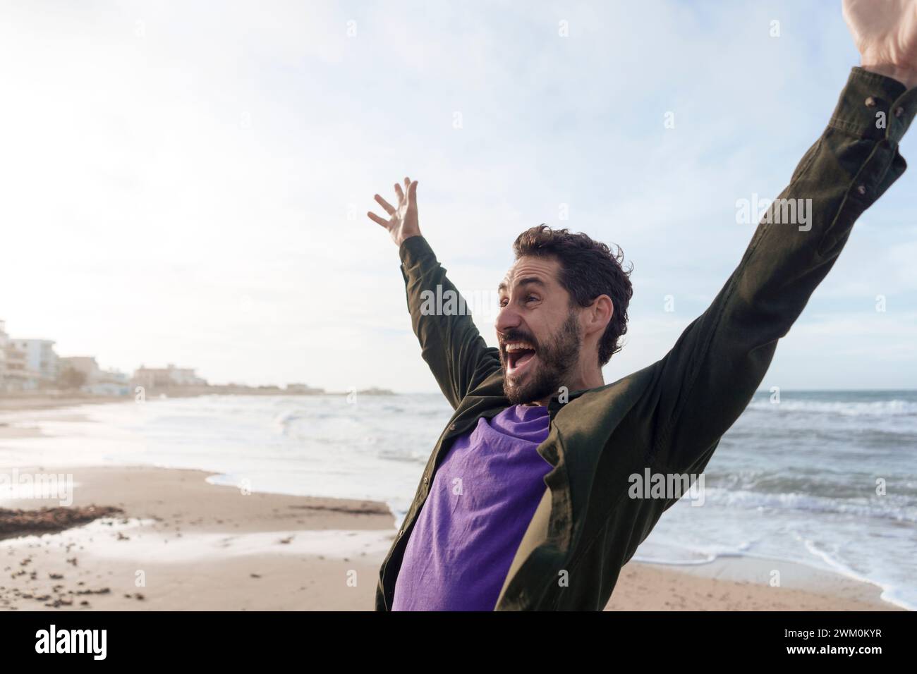 Uomo spensierato che si diverte con le braccia sollevate in spiaggia Foto Stock