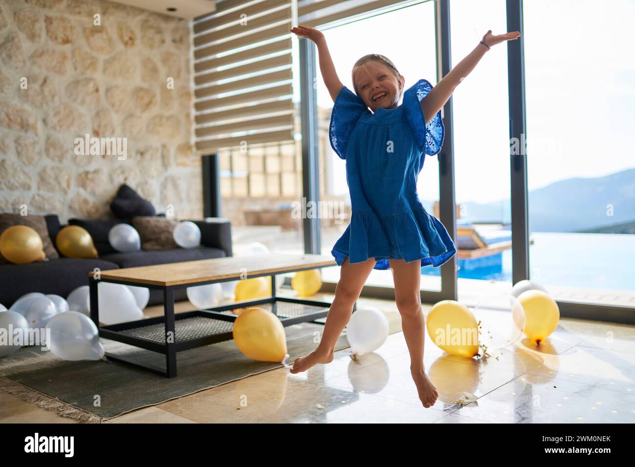 Ragazza felice che salta con le braccia sollevate da palloncini sul pavimento della villa Foto Stock