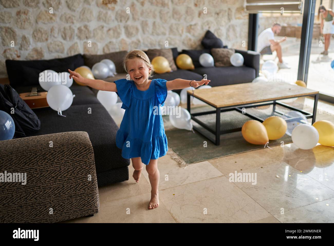 Ragazza felice in piedi con le braccia allungate con palloncini di compleanno nel soggiorno della villa Foto Stock