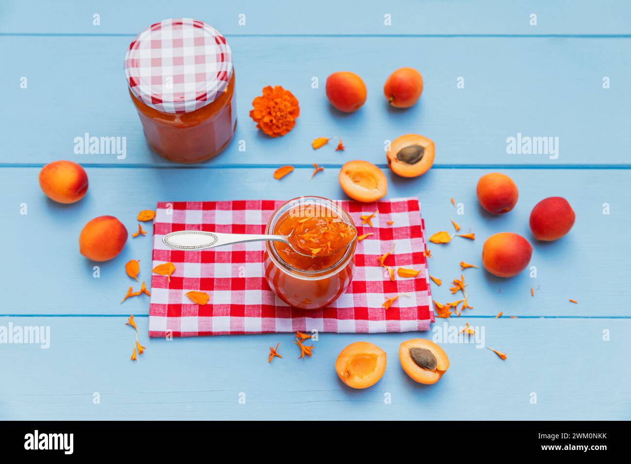 Marmellata di albicocche fatta in casa con petali di calendula e albicocche crude su legno blu Foto Stock