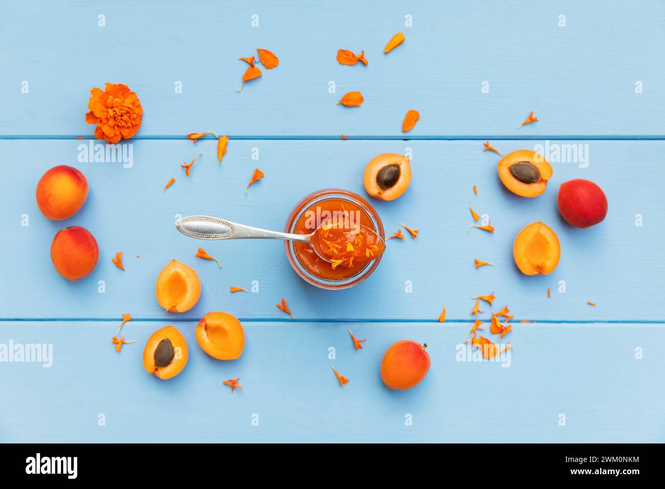 Marmellata di albicocche fatta in casa con petali di calendula e albicocche crude su legno blu Foto Stock