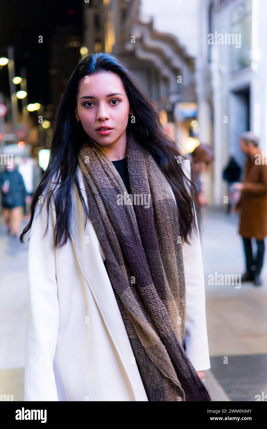 Giovane donna con lunghi capelli neri in piedi in strada in città Foto Stock