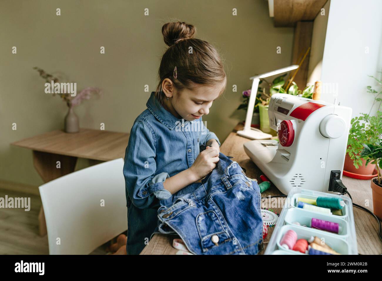 Ragazza sorridente che taglia vecchi vestiti con la macchina da cucire a casa Foto Stock