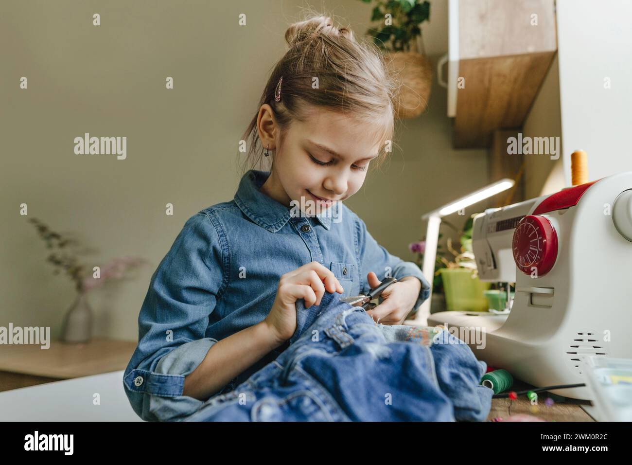 Ragazza sorridente che taglia il panno con le forbici a casa Foto Stock