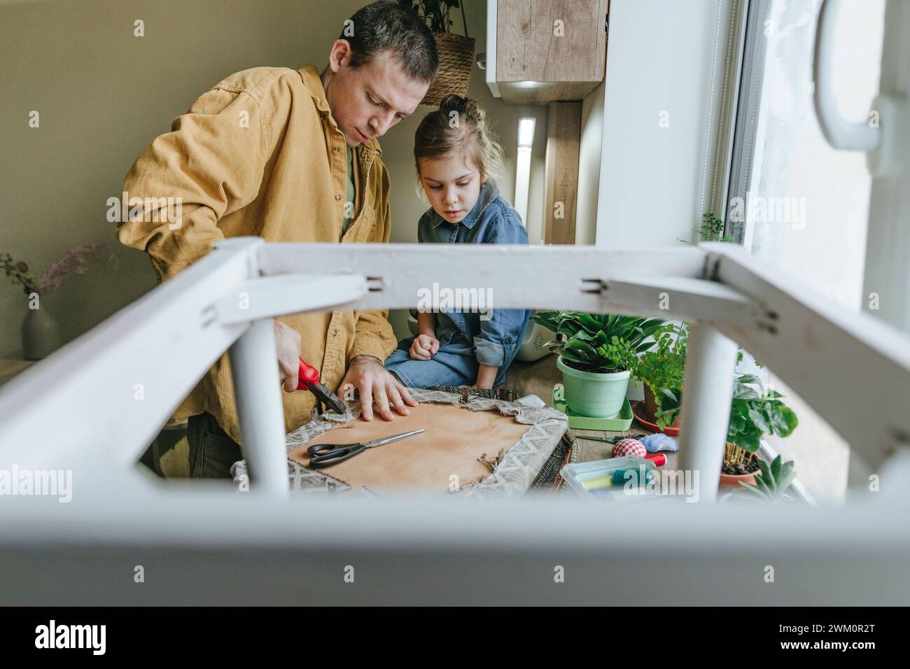 Figlia con padre che rimuove il vecchio tessuto dalla sedia per il upcycling Foto Stock