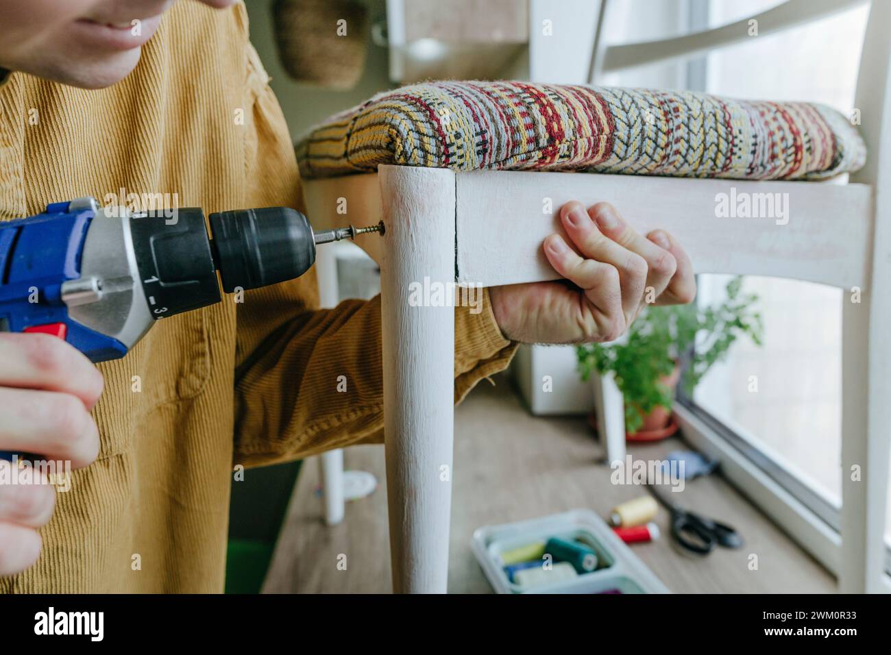 Uomo che utilizza un cacciavite trapano sulla sedia a casa Foto Stock