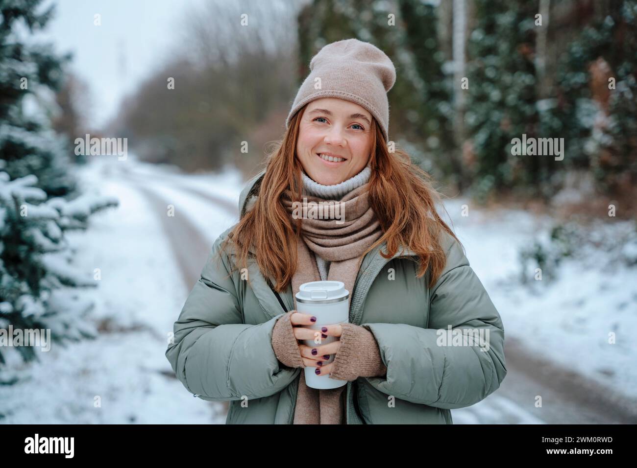 Donna sorridente che indossa abiti caldi e tiene in mano termos Foto Stock