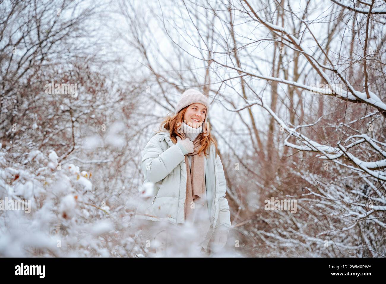 Donna sorridente che trascorre il tempo libero tra alberi ghiacciati in inverno Foto Stock