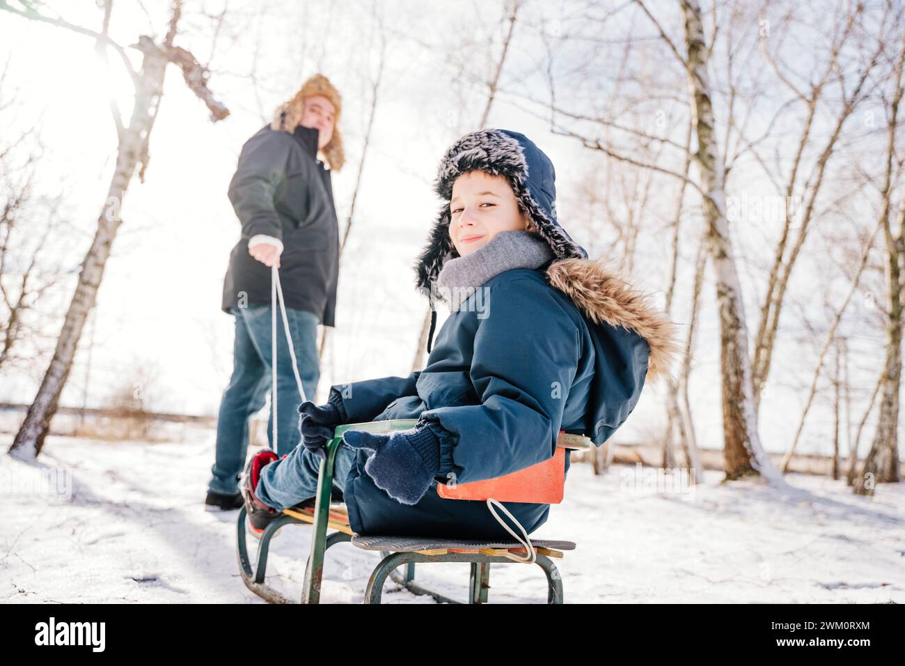 Ragazzo sorridente che guarda dietro la spalla seduto sulla slitta in inverno Foto Stock