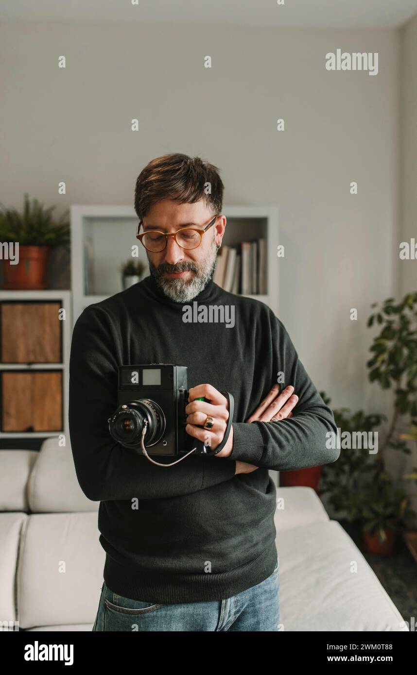 Uomo con una vecchia fotocamera istantanea in piedi a casa Foto Stock