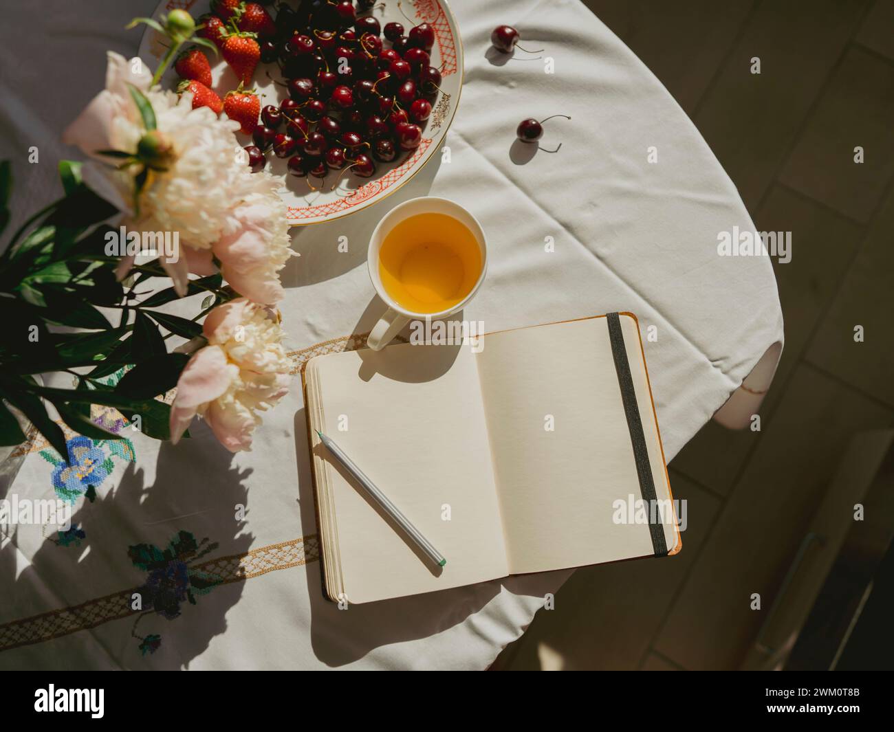 Apri il diario vicino alla tazza da tè e alle ciliegie sul tavolo a casa Foto Stock