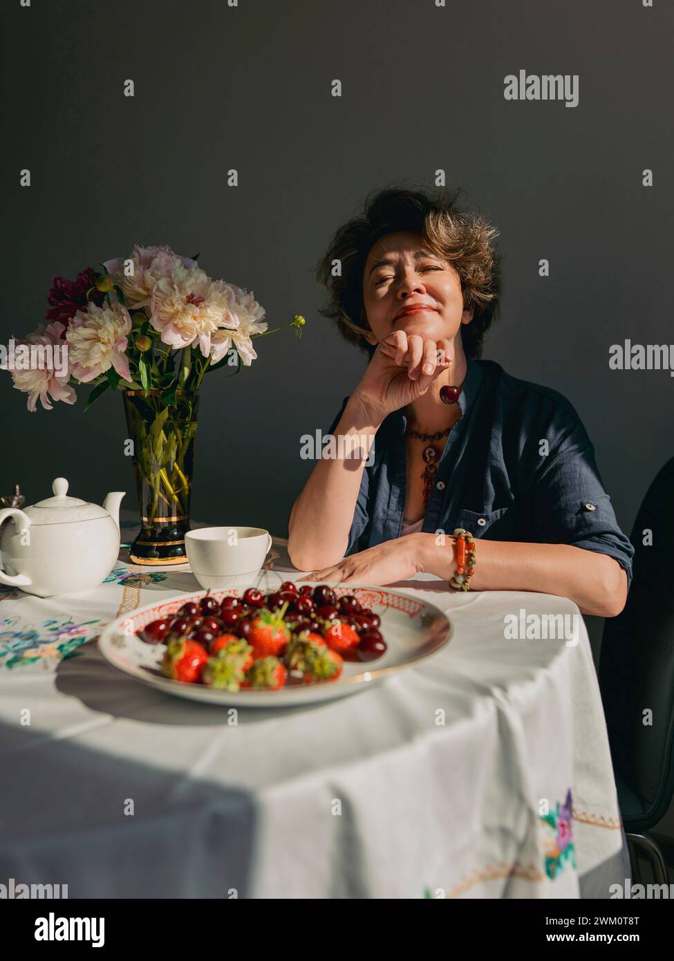 Donna matura sorridente seduta con tè e frutta a casa Foto Stock