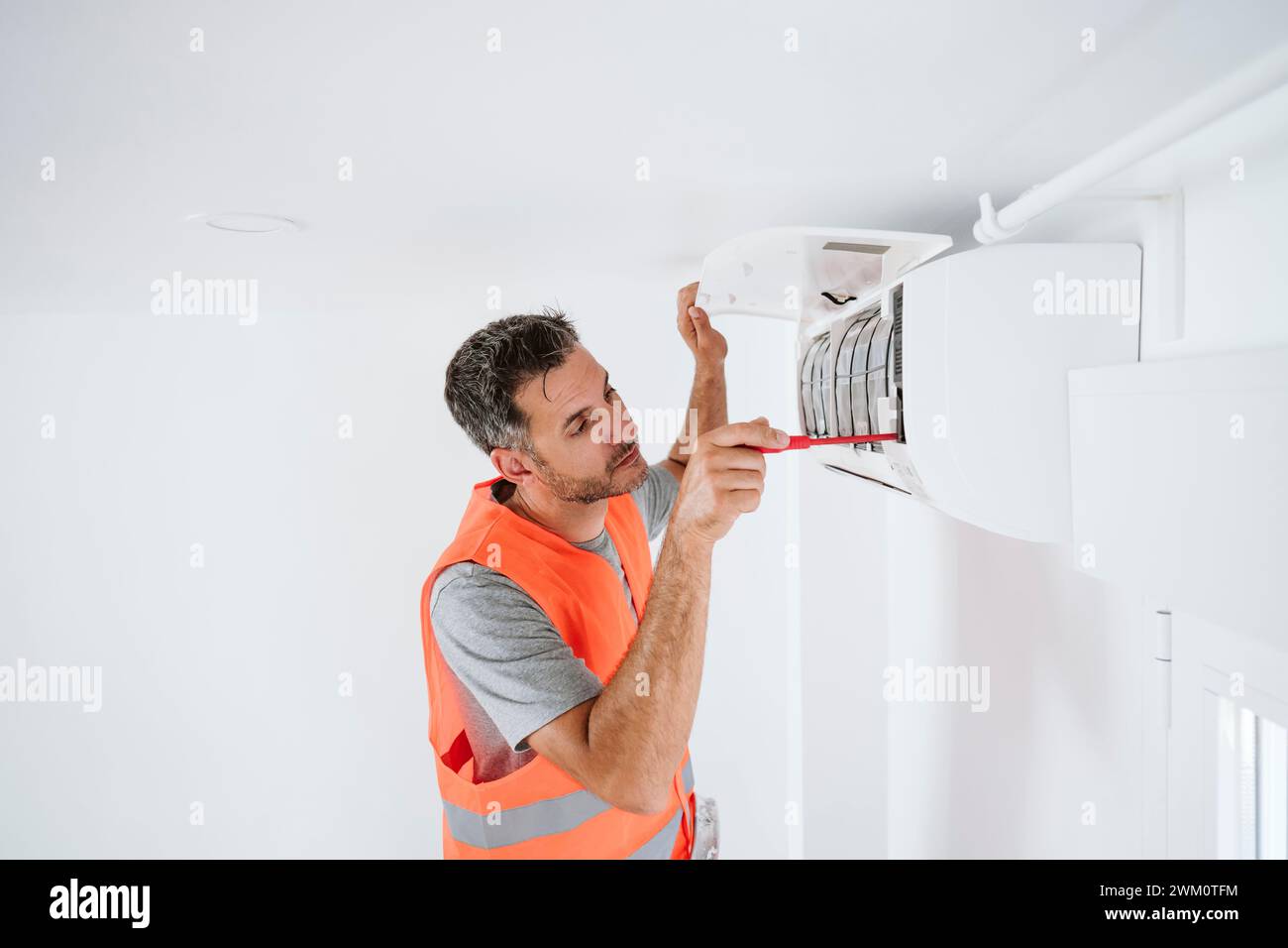 Tecnico maturo che ripara il climatizzatore a casa Foto Stock