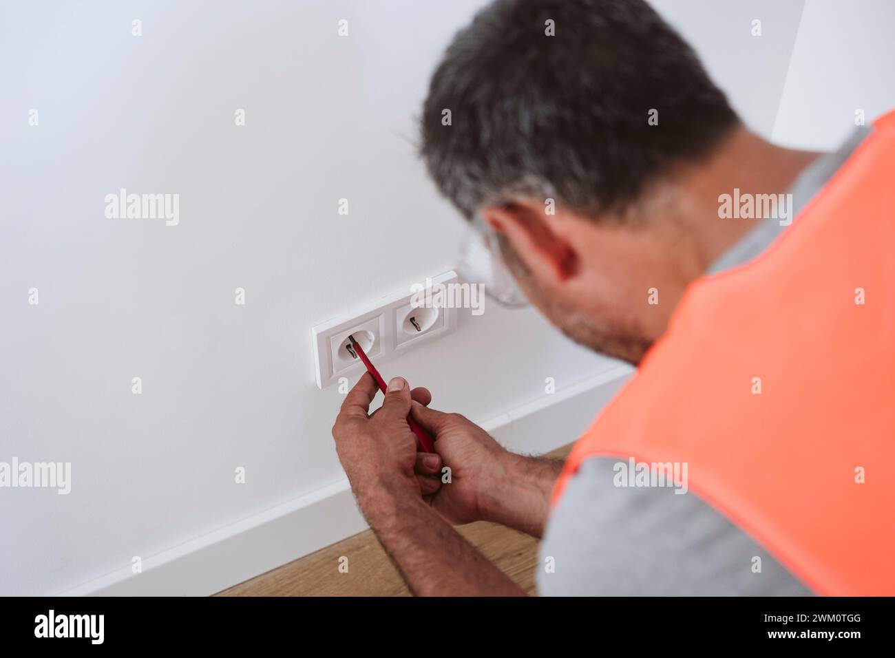 Tecnico maturo che ripara la presa elettrica a casa Foto Stock