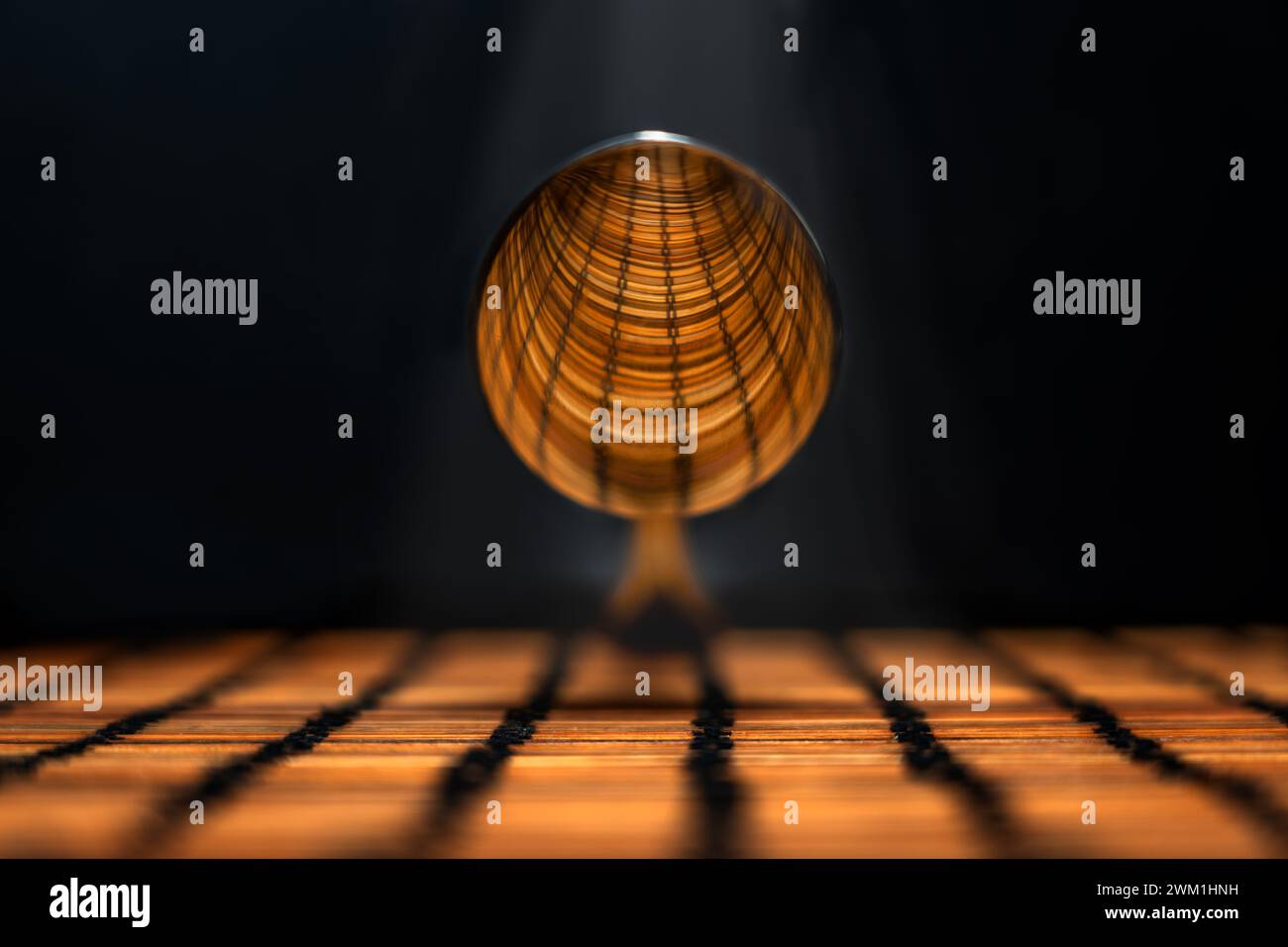 immagine della parte convessa di un cucchiaio d'argento sospeso che riflette il disegno lineare del piano sottostante, illuminato da un raggio di luce dall'alto Foto Stock