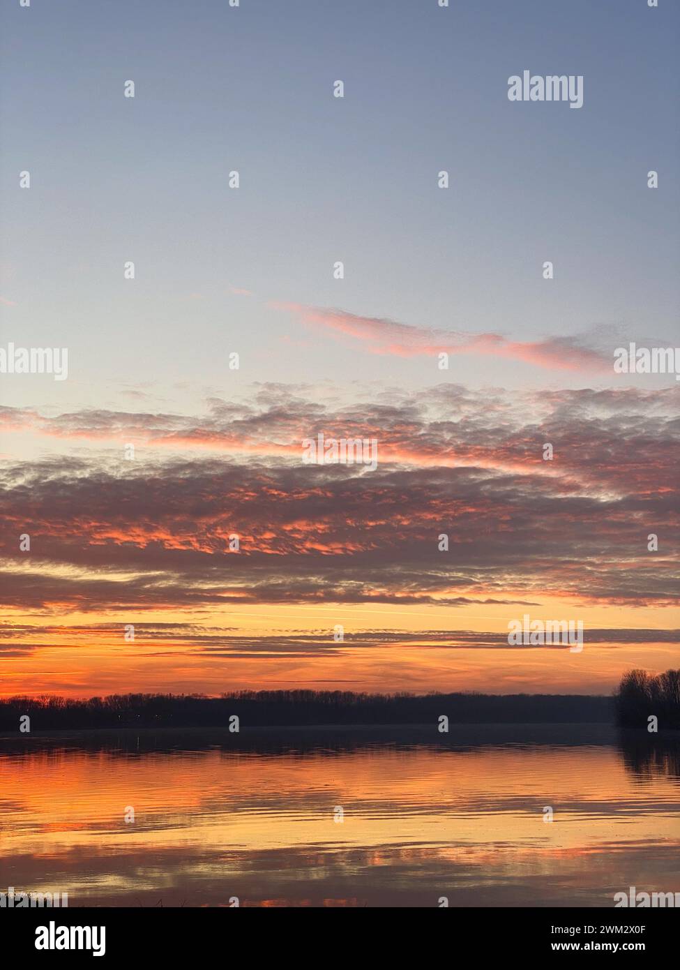 Fiume po e vibrante tramonto sullo sfondo. Il cielo è dipinto in sfumature di arancione, che riflettono l'acqua increspata. San Nazzaro, PC, Italia Foto Stock