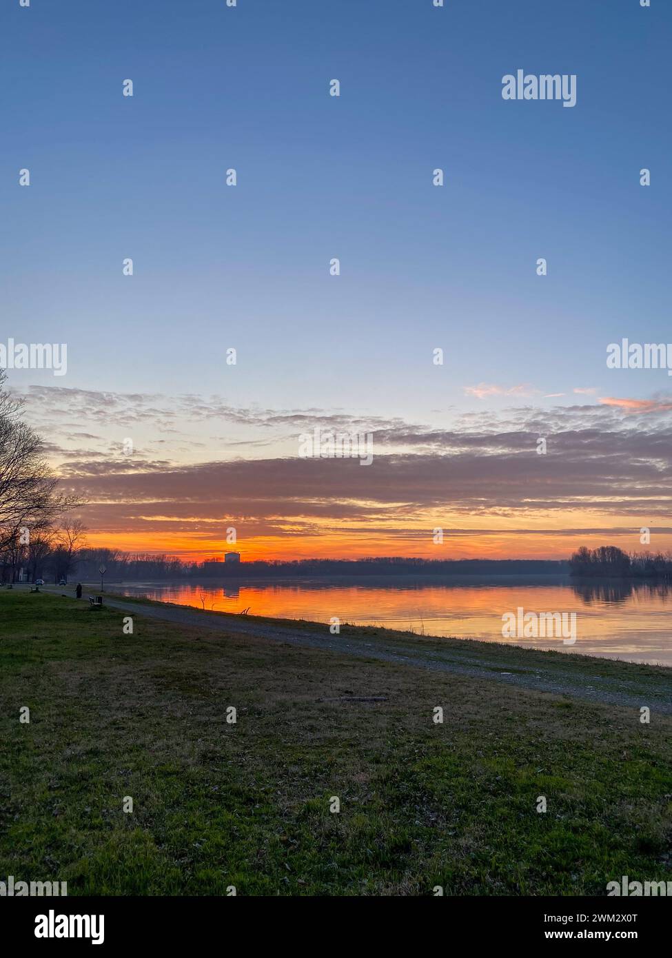 Fiume po e vibrante tramonto sullo sfondo. Il cielo è dipinto in sfumature di arancione, che riflettono l'acqua increspata. San Nazzaro, PC, Italia Foto Stock