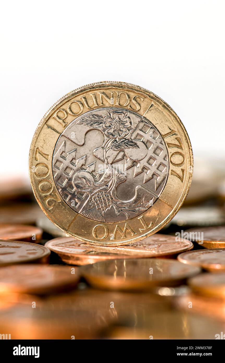 Foto in studio di una moneta da due sterline in valuta Sterling in piedi sul tavolo con monete sfocate in primo piano su sfondo bianco Foto Stock