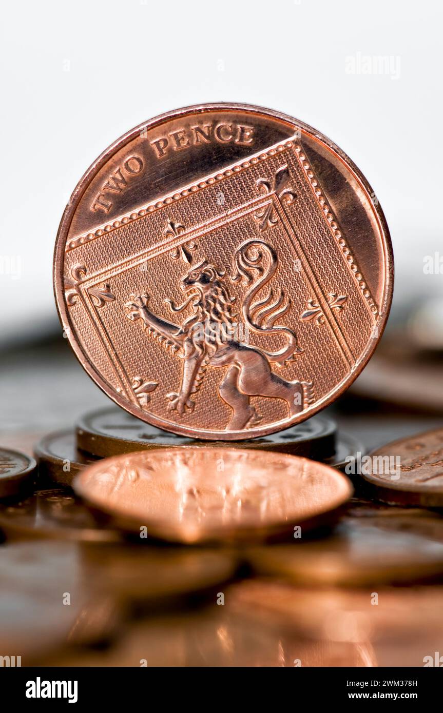 Foto in studio di un pezzo da due pence in valuta Sterling in piedi sul tavolo con monete sfocate in primo piano su sfondo bianco Foto Stock