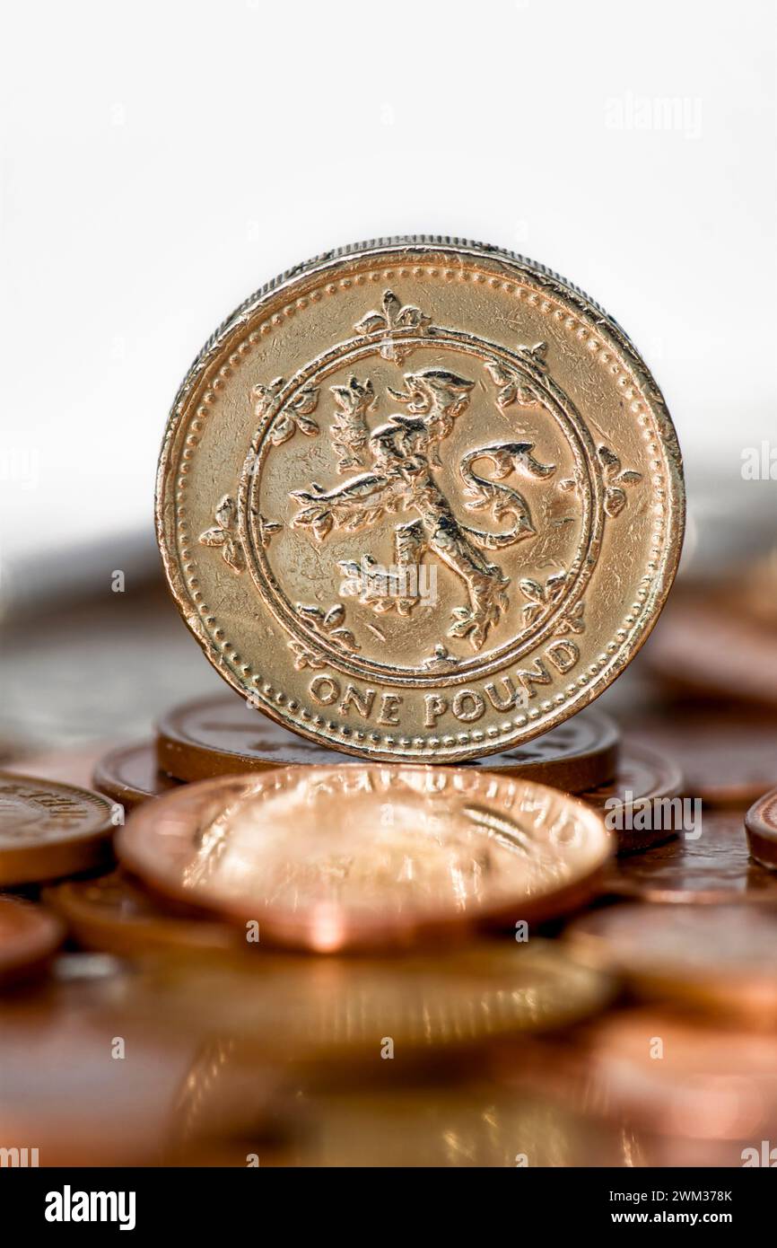 Scatto in studio di una moneta da un libbra in valuta Sterling in piedi sul tavolo con monete sfocate in primo piano su sfondo bianco Foto Stock
