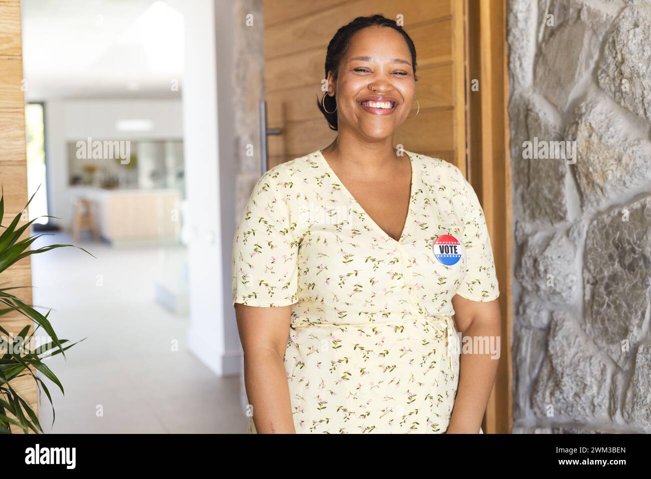Una giovane donna birazziale sorridente si trova in un corridoio luminoso, indossando un distintivo di voto, con spazio per le copie Foto Stock