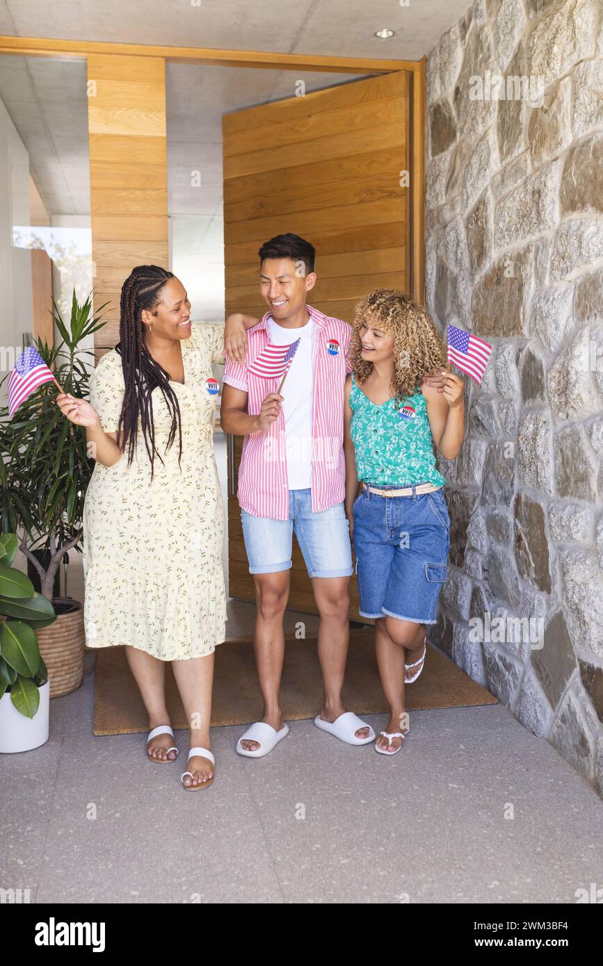 Il giovane asiatico e due giovani donne birazziali festeggiano con bandiere americane, indossando distintivi di voto Foto Stock