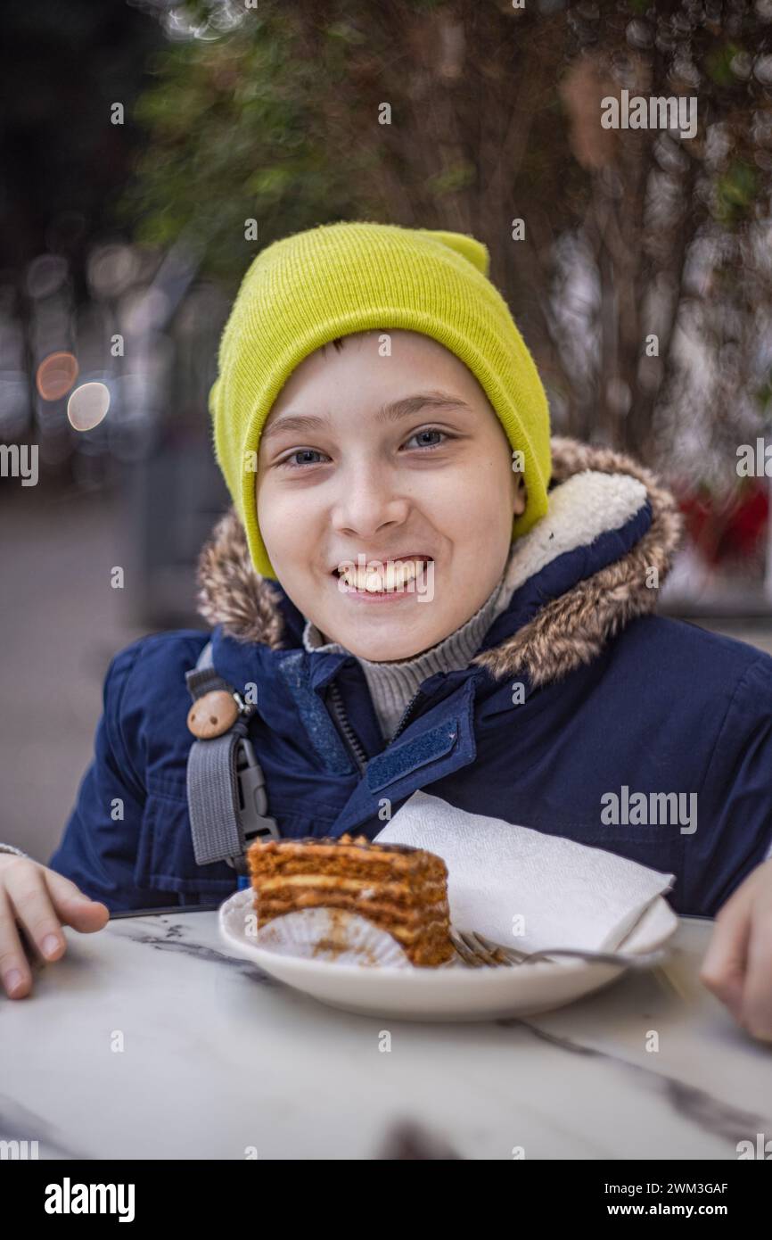 Bel ragazzo che mangia la torta nel caffè all'aperto Foto Stock